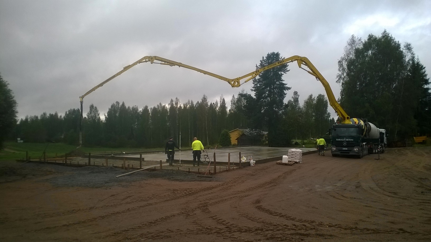 Betonipumppuauton puomi ulottuu kauas työmaalla metsän reunassa